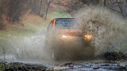 Front view of a Jeep-style 4x4 creating a dramatic mud plume during a creek crossing.