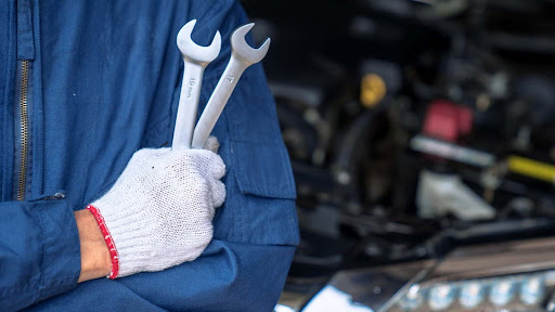 Auto mechanic gripping two combination wrenches beside a vehicle in service