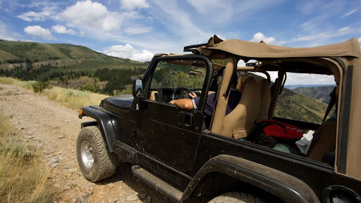Open-air Jeep with tan interior overlooking rolling hills and blue sky.
