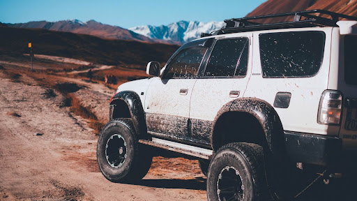 Lifted white 4x4 SUV with mud-splattered doors parked on a dirt trail in the mountains.