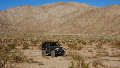 Black Jeep Wrangler parked in a wide desert basin with scrub and mountains.